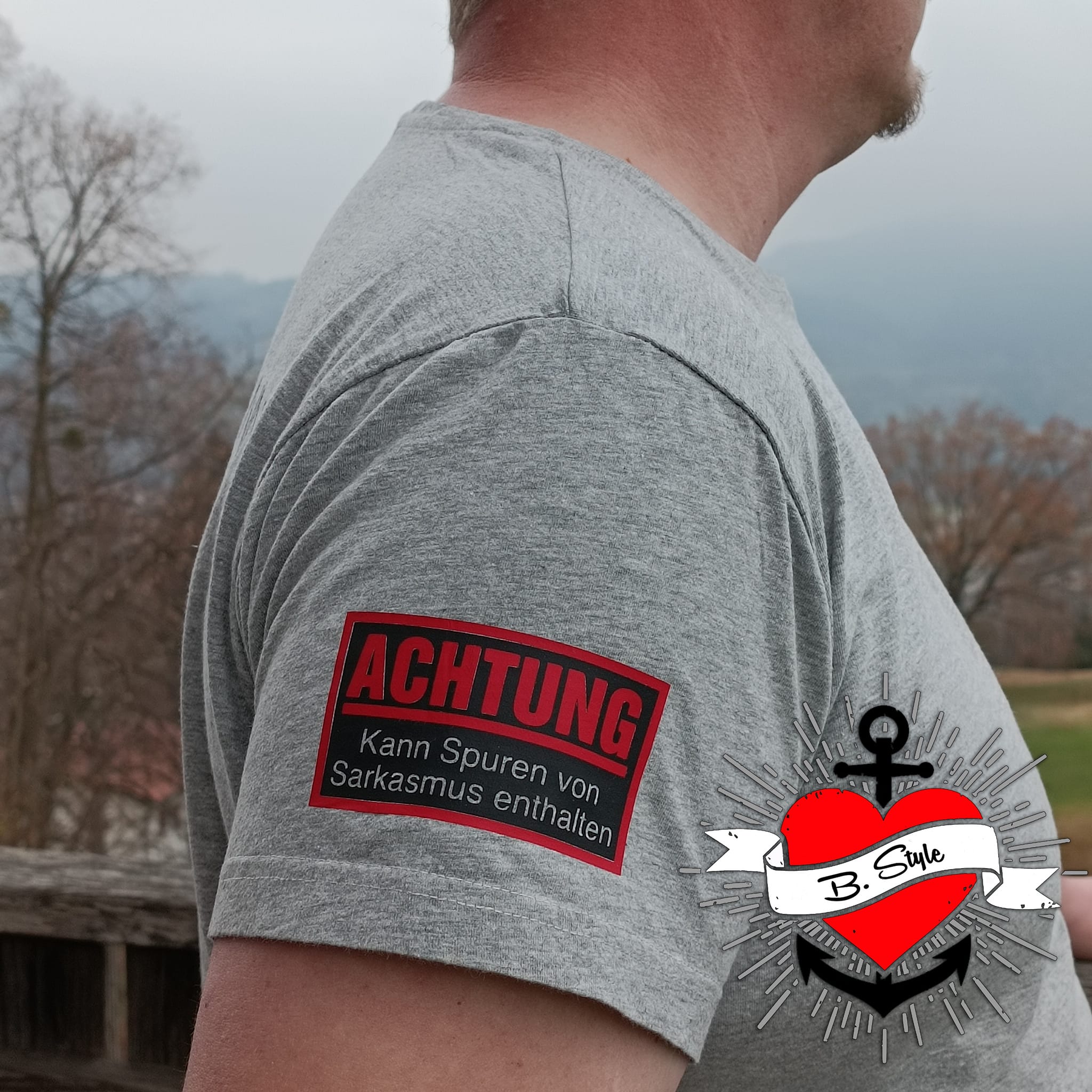 Seitenansicht eines grauen T-Shirts mit der Aufschrift "Achtung - Kann Spuren von Sarkasmus enthalten" von easy-sticks, das für humorvolle Statement-Kleidung steht.