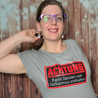 Portrait einer Person in einem grauen T-Shirt mit dem Aufdruck 'Achtung - Kann Spuren von Sarkasmus enthalten' von easy-sticks, ideal für kreative Projekte.