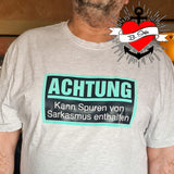 Ein Mann trägt ein graues T-Shirt mit der Aufschrift "Achtung - Kann Spuren von Sarkasmus enthalten" von easy-sticks, ideal für humorvolle Anlässe.