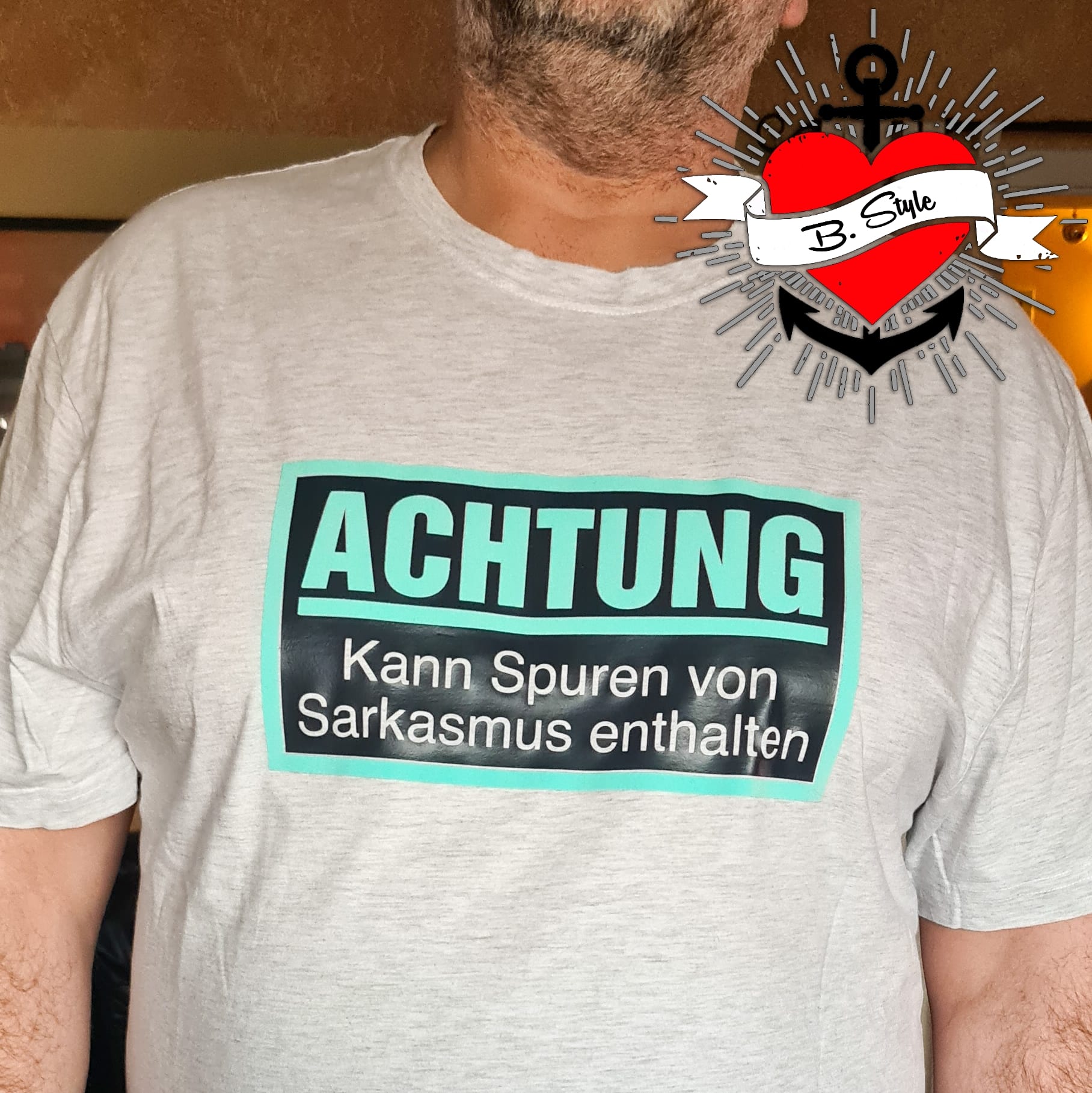 Ein Mann trägt ein graues T-Shirt mit der Aufschrift "Achtung - Kann Spuren von Sarkasmus enthalten" von easy-sticks, ideal für humorvolle Anlässe.