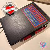 Schwarzes Notizbuch mit dem Aufdruck 'Achtung - Kann Spuren von Sarkasmus enthalten' von easy-sticks, ergänzt durch einen roten Stift, eine originelle Idee für kreative Notizen.