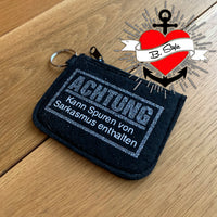 Schwarze Geldbörse mit Glitzer und der Aufschrift "Achtung - Kann Spuren von Sarkasmus enthalten" von easy-sticks, perfekt für kreative Menschen.