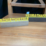 Bunte Plotter-Worte 'Schietwetter' und 'Heimathafen' auf einem Holzsockel, kreativ gestaltet von easy-sticks.