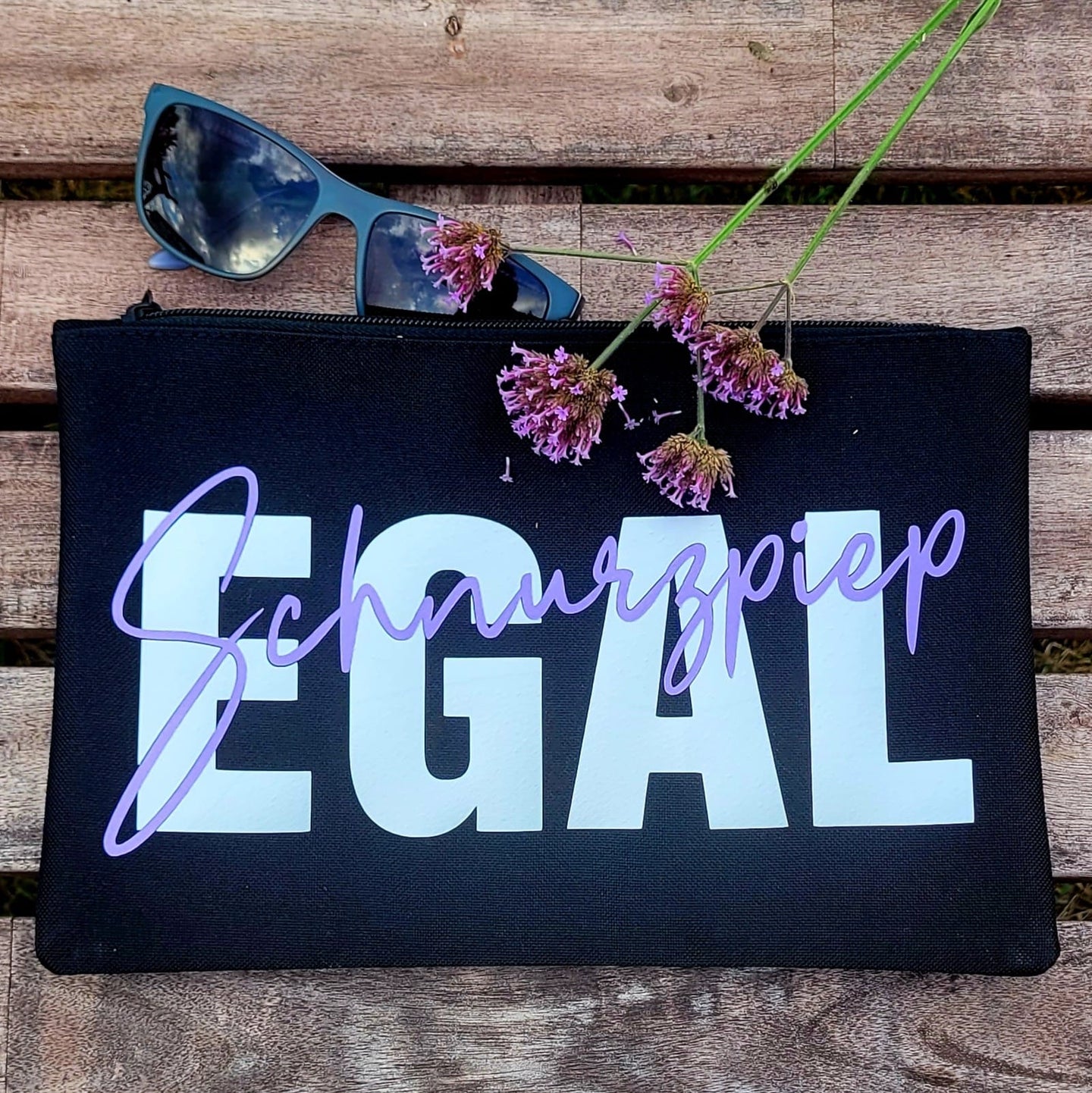 Stylisches Täschchen mit der "Schnurzpiep Egal" Plotterdatei von easy-sticks, das den Schriftzug "Schnurzpiep" in elegantem Lila und "Egal" in Weiß zeigt, auf einem Holzuntergrund.