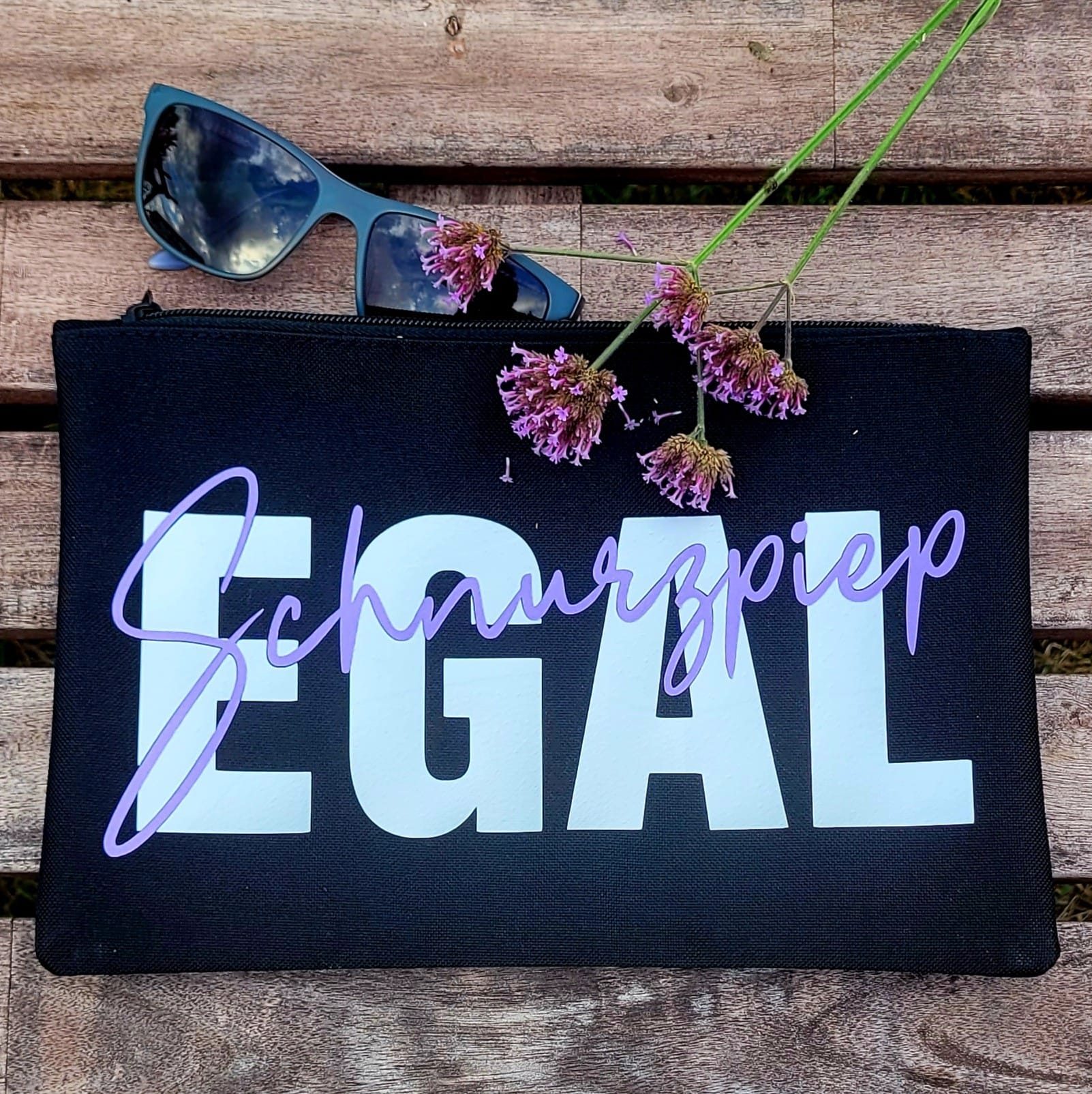 Stylisches Täschchen mit der "Schnurzpiep Egal" Plotterdatei von easy-sticks, das den Schriftzug "Schnurzpiep" in elegantem Lila und "Egal" in Weiß zeigt, auf einem Holzuntergrund.