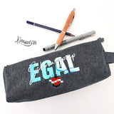 Ein graues Federmäppchen, verziert mit dem Spruch "Schnurzpiep Egal" in lebendigen Blau- und Weißtönen. Ein tolles Ergebnis der Plotterdatei von easy-sticks.
