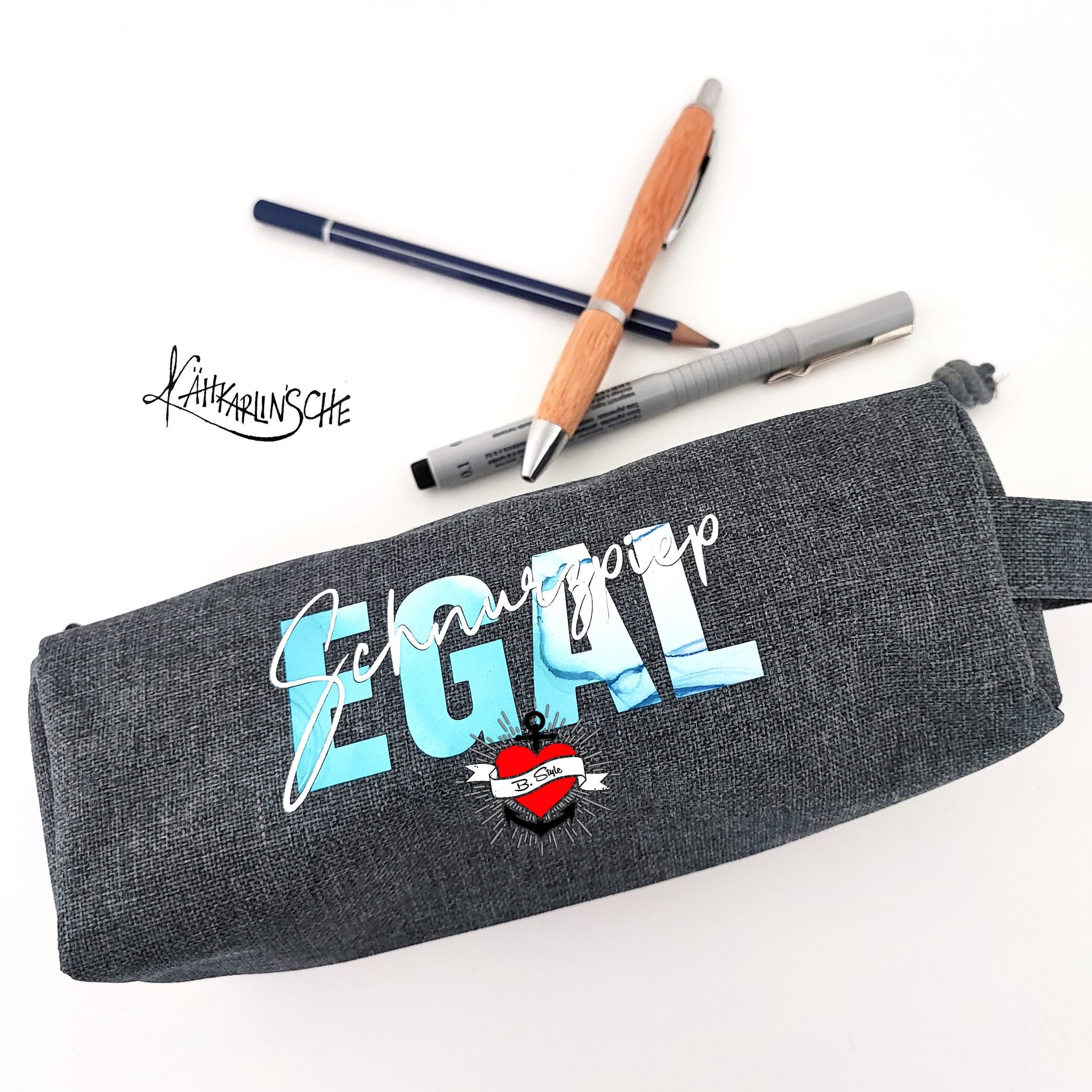 Ein graues Federmäppchen, verziert mit dem Spruch "Schnurzpiep Egal" in lebendigen Blau- und Weißtönen. Ein tolles Ergebnis der Plotterdatei von easy-sticks.
