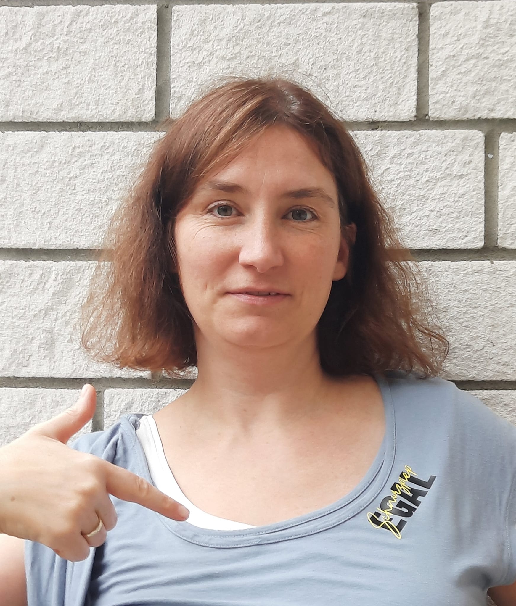 Eine Frau zeigt stolz auf ihren T-Shirt Aufdruck mit der Aufschrift 'Schnurzpiep Egal', ideal für kreative Projekte. Die Bilddatei gehört zur 'Schnurzpiep Egal' Plotterdatei von easy-sticks, die vielseitige Anwendungen für Plottarbeiten bietet.
