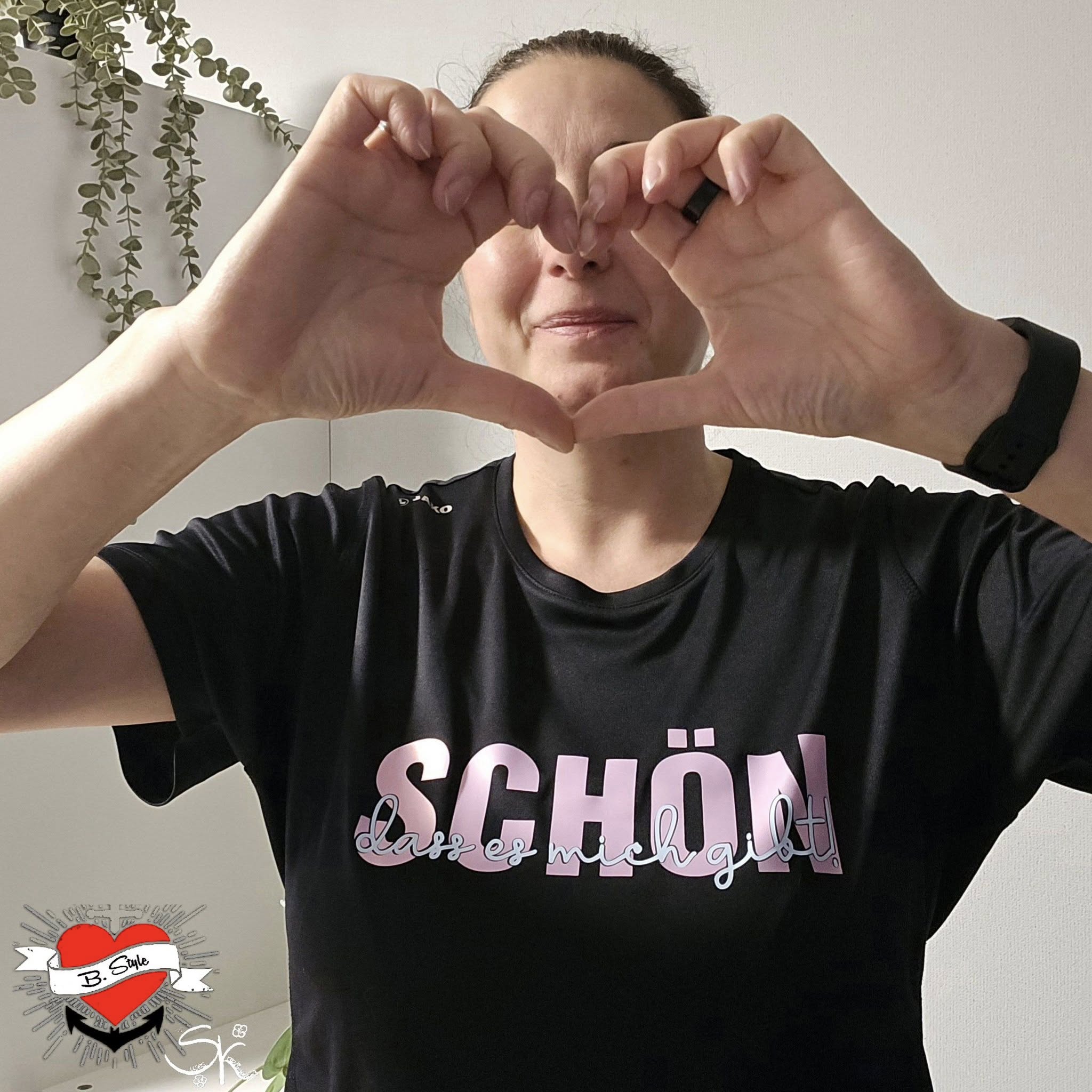Frau in schwarzem T-Shirt mit dem Aufdruck "Schön, dass es mich gibt" und Herzform aus ihren Händen, entworfen von easy-sticks, inspiriert von der Plotterdatei.