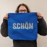 Eine kreative Person hält eine blaue Tasche mit dem Design "Schön, dass es mich gibt". Diese Plotterdatei von easy-sticks ermöglicht es, einzigartige Produkte zu gestalten.