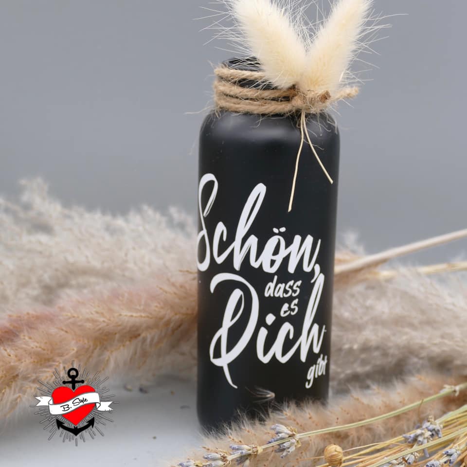 Eine elegante schwarze Vase mit der Aufschrift "Schön, dass es dich gibt" von easy-sticks. Diese inspirierende Gestaltung ist ideal für kreative Projekte mit der Plotterdatei. Die Vase wird von Trockenblumen umgeben und verleiht jedem Raum eine persönliche Note.