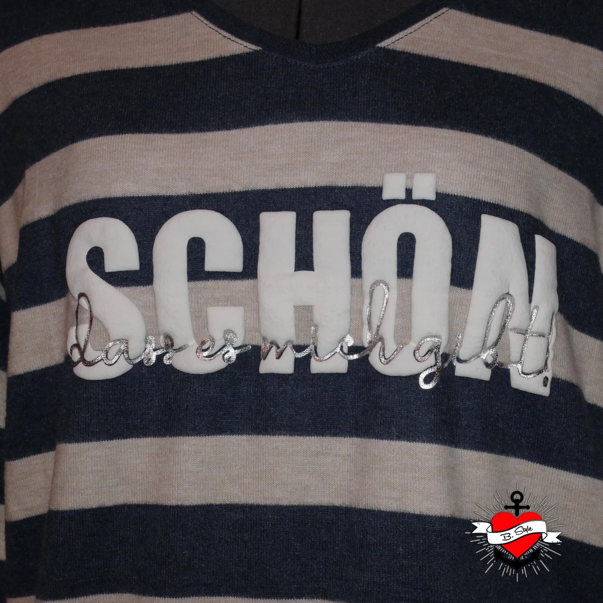 Ein gestreiftes Oberteil, auf dem der Schriftzug "Schön, dass es mich gibt" in Weiß und Silber zu sehen ist. Diese Plotterdatei von easy-sticks bringt persönliche Note in kreative Kleidung.