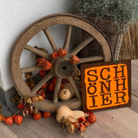 Die rustikale Präsentation der "SCHÖN HIER" Plotterdatei von easy-sticks, die als Deko-Element an einem Wagenrad mit herbstlichen Akzenten platziert wurde.