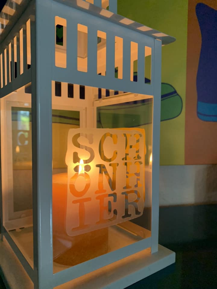 Eine dekorative Laterne mit dem Schriftzug "SCHÖN HIER" aus der Plotterdatei von easy-sticks, die einen warmen Lichtschein im Hintergrund erzeugt.