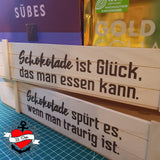 Schokolade Sprüche Plotterdatei von easy-sticks, eine Holzbox mit inspirierenden Sprüchen über Schokolade, umgeben von Schokoladenverpackungen.