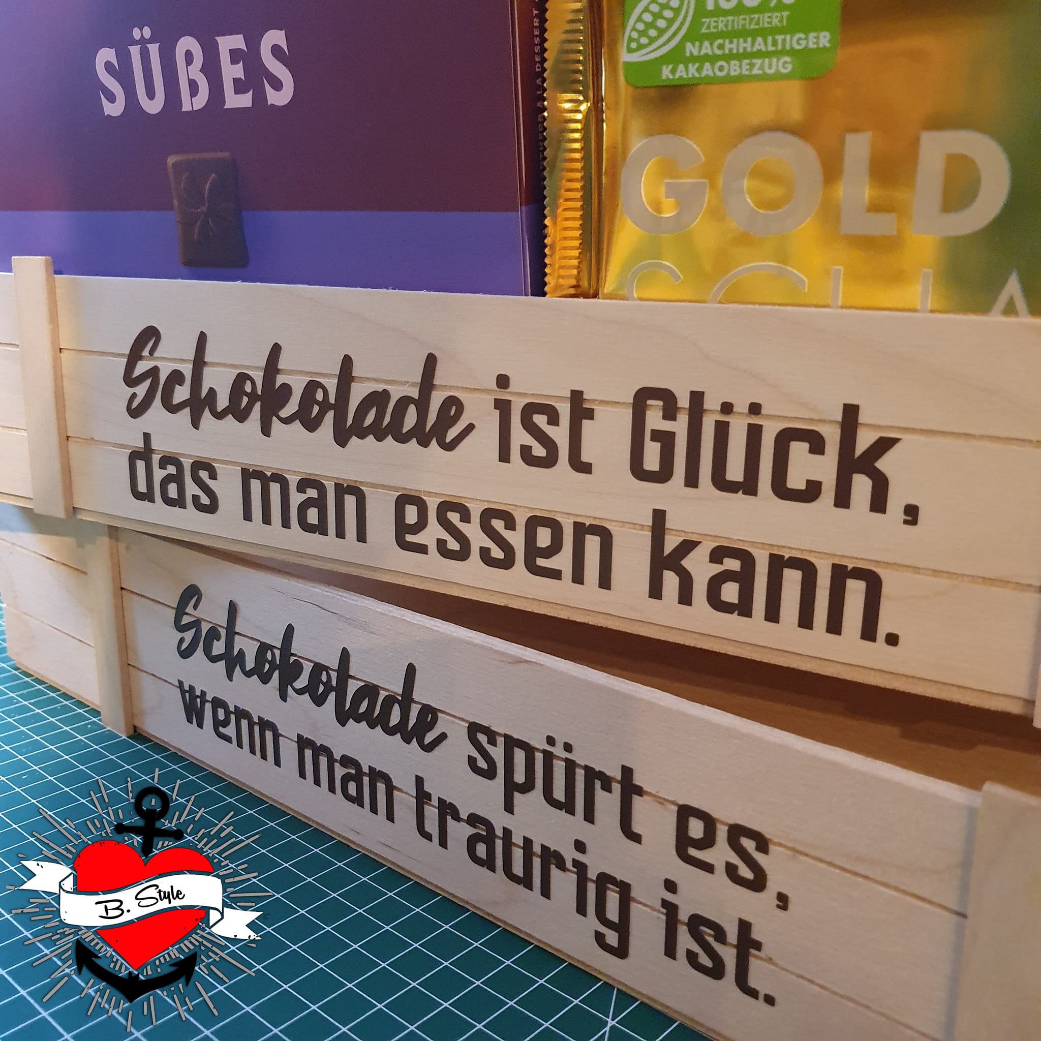 Schokolade Sprüche Plotterdatei von easy-sticks, eine Holzbox mit inspirierenden Sprüchen über Schokolade, umgeben von Schokoladenverpackungen.