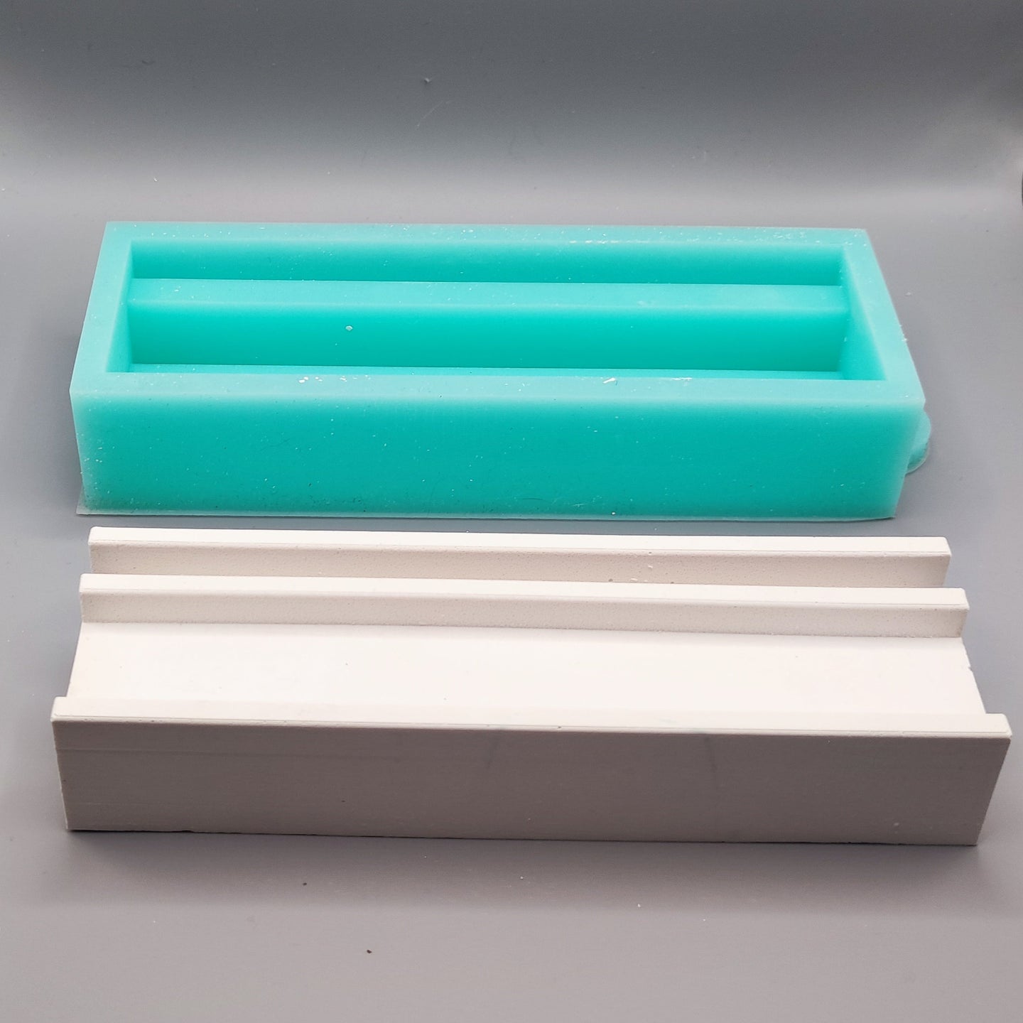 Zwei Silikonformen, darunter die Easy-Sticks Silikonform Basis für Einschieber in mintgrün und eine weitere in weiß auf grauem Hintergrund.