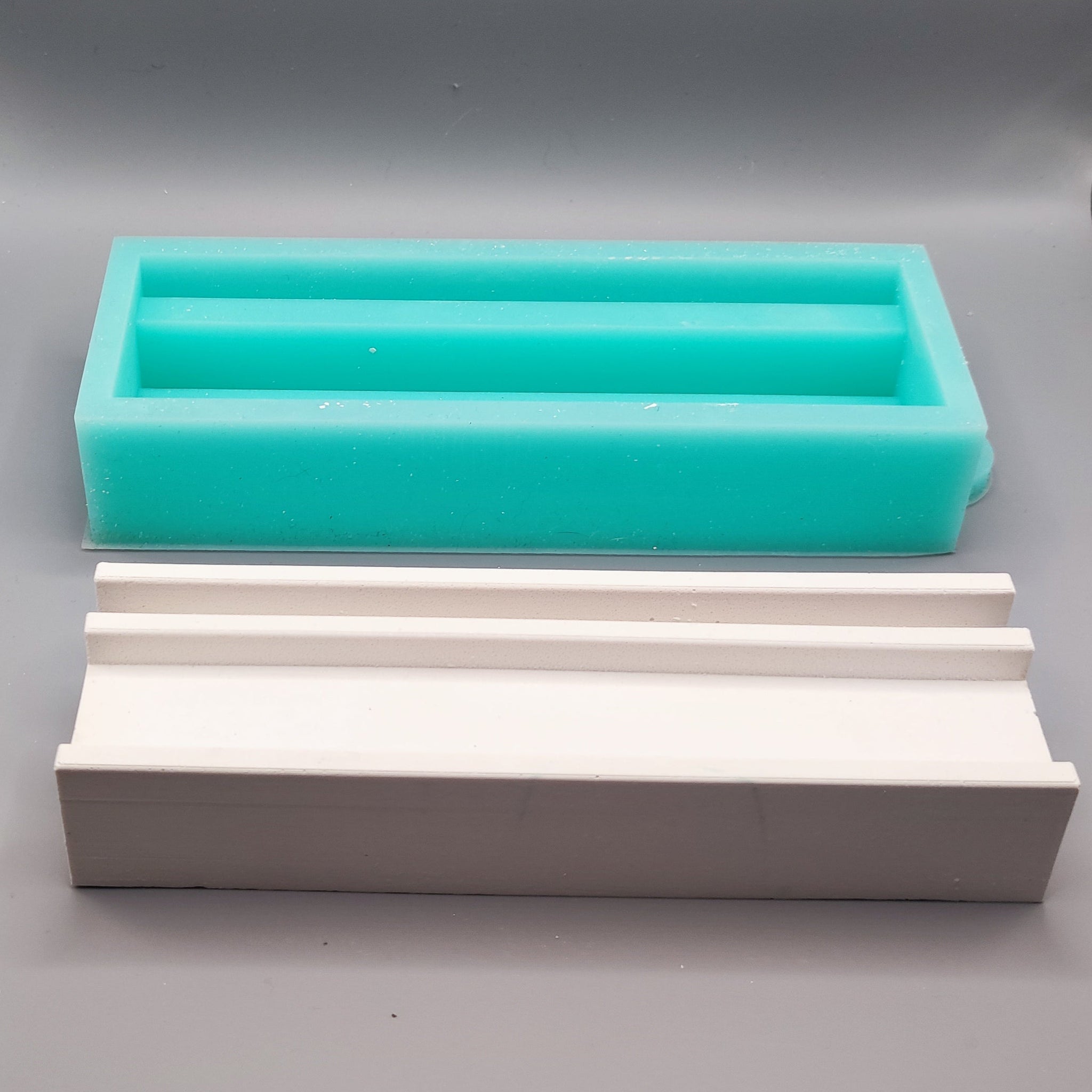 Zwei Silikonformen, darunter die Easy-Sticks Silikonform Basis für Einschieber in mintgrün und eine weitere in weiß auf grauem Hintergrund.