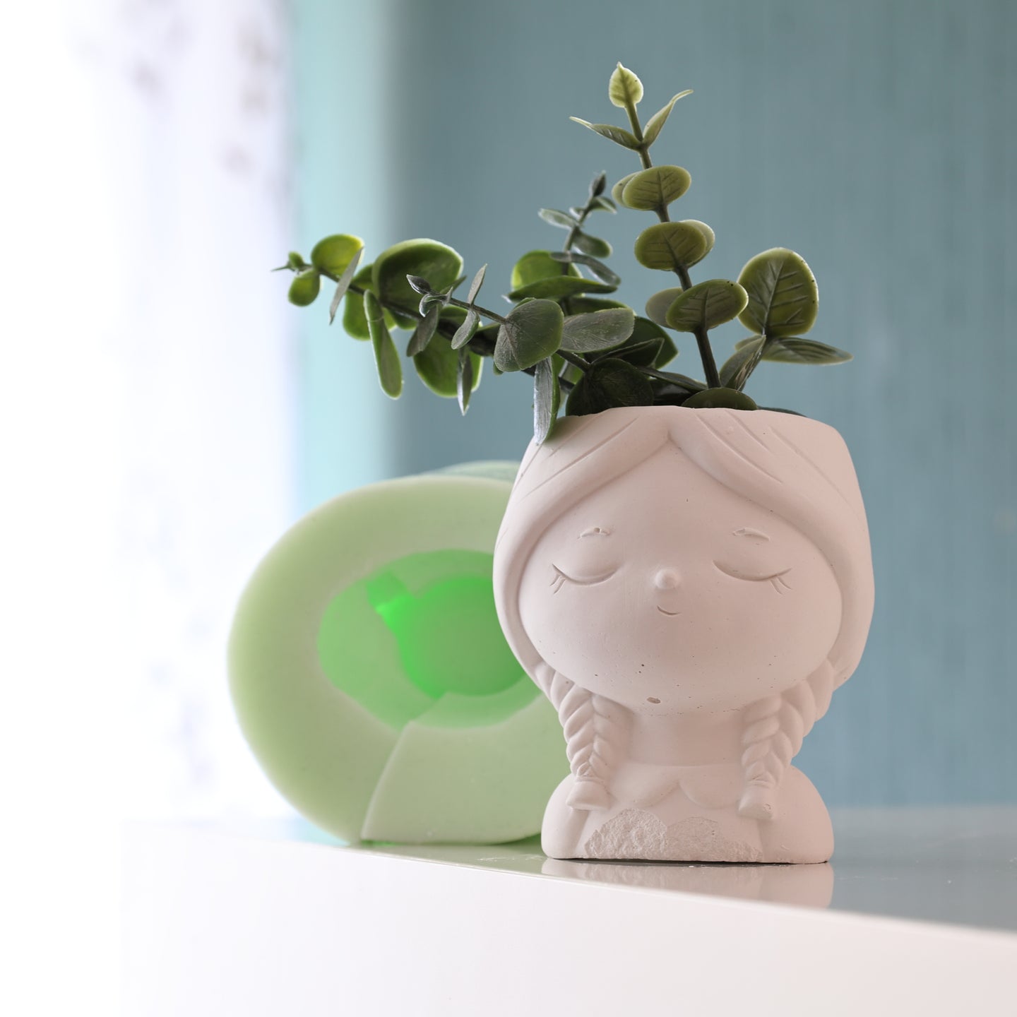 Charmanter Mädchen-mit-Zöpfen-Blumentopf von easy-sticks, präsentiert mit dekorativen Pflanzen auf einem modernen Hintergrund.