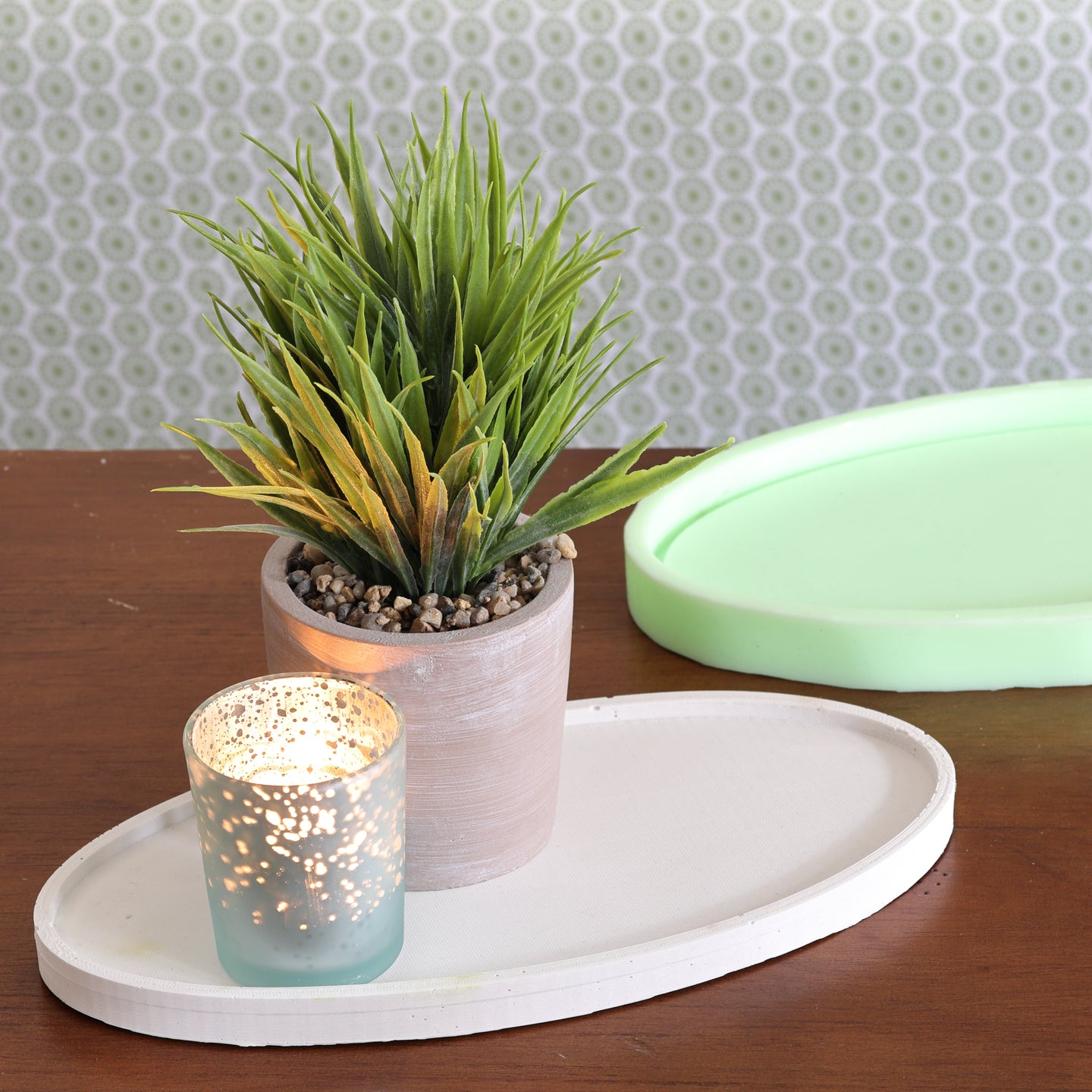 Ovales Tablett Silikonform von easy-sticks, dekorativ arrangiert mit einer Kunstpflanze und einem leuchtenden Teelicht, auf einem Tisch mit zusätzlichem Silikonform-Hintergrund.