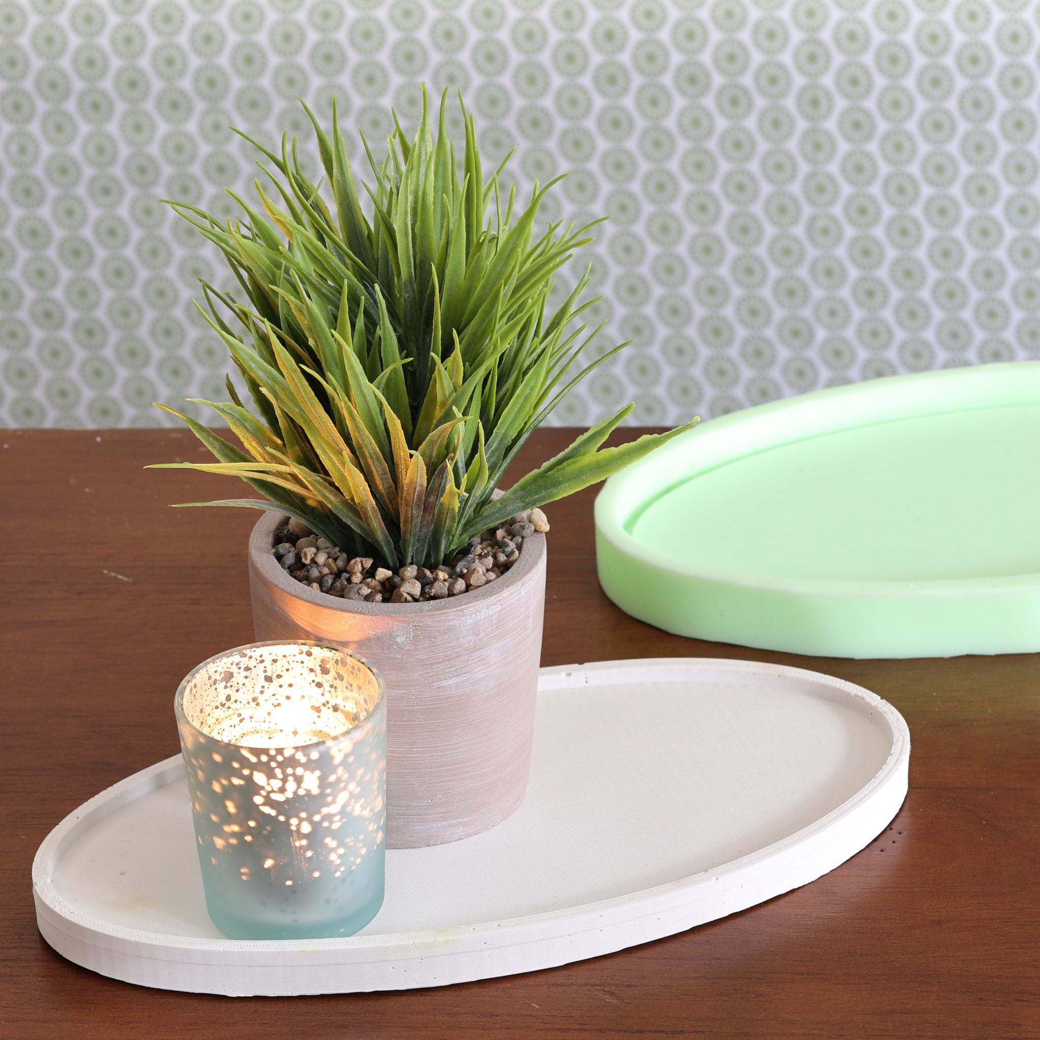 Ovales Tablett Silikonform von easy-sticks, dekorativ arrangiert mit einer Kunstpflanze und einem leuchtenden Teelicht, auf einem Tisch mit zusätzlichem Silikonform-Hintergrund.
