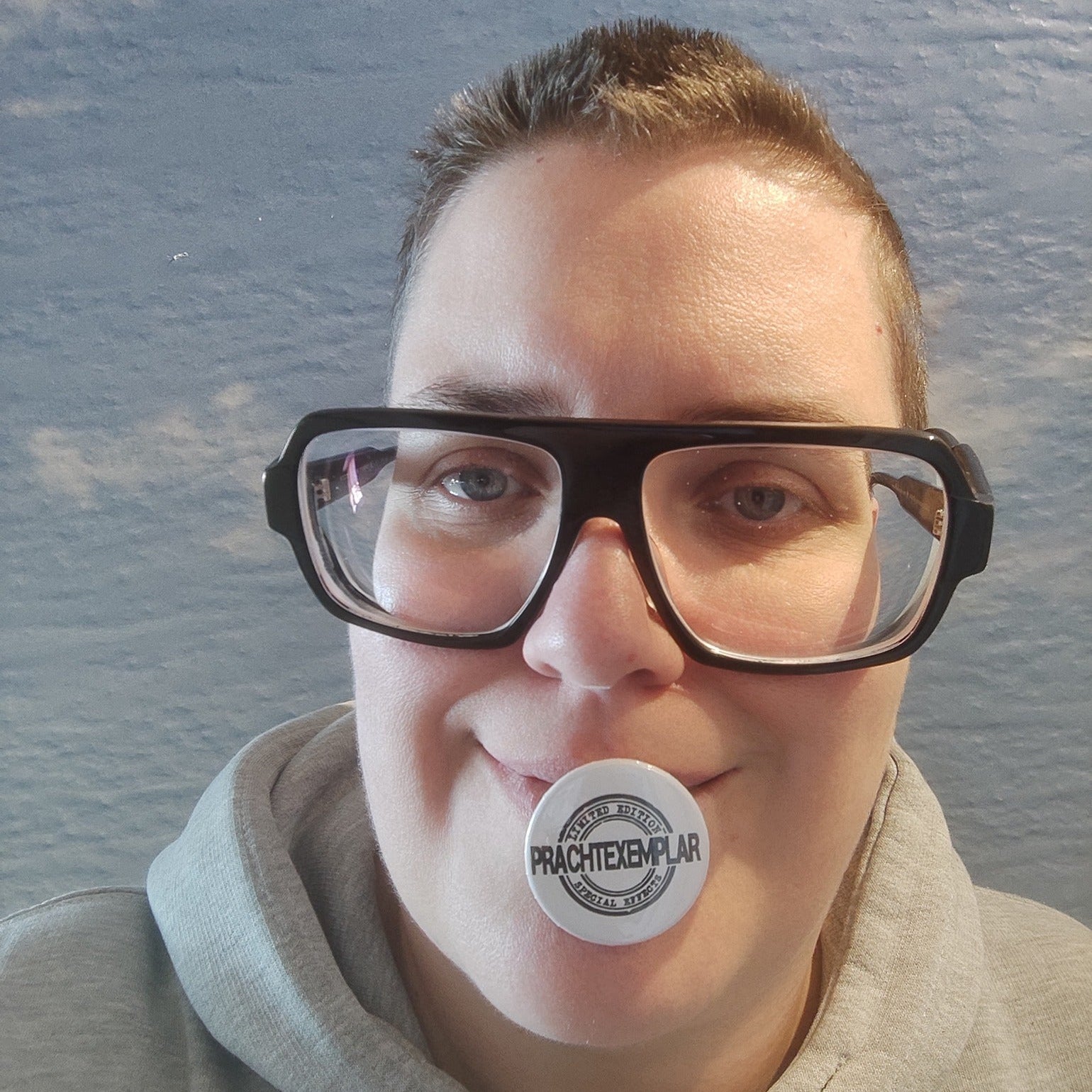 Eine Person mit großen Brillen, die stolz einen Prachtexemplar Button hält, kreiert von easy-sticks.