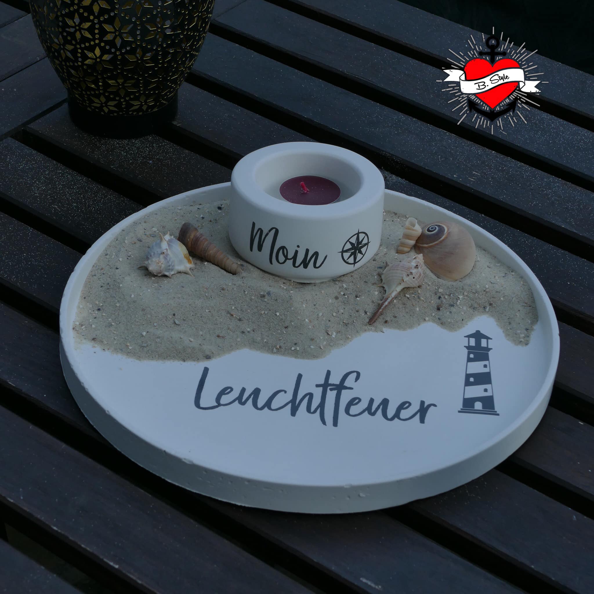 Moderne Tischdekoration mit der Sommer und Urlaub Sprüche Plotterdatei von easy-sticks: Eine elegante Sand- und Kerzenanordnung mit Leuchtfeuer-Motiv und Muscheln.