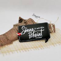 Schwarzes Schild mit dem Spruch "Die Sonne ist auch alleine und scheint trotzdem" auf natürlichem Untergrund, perfektes Accessoire für persönliche Projekte von easy-sticks.