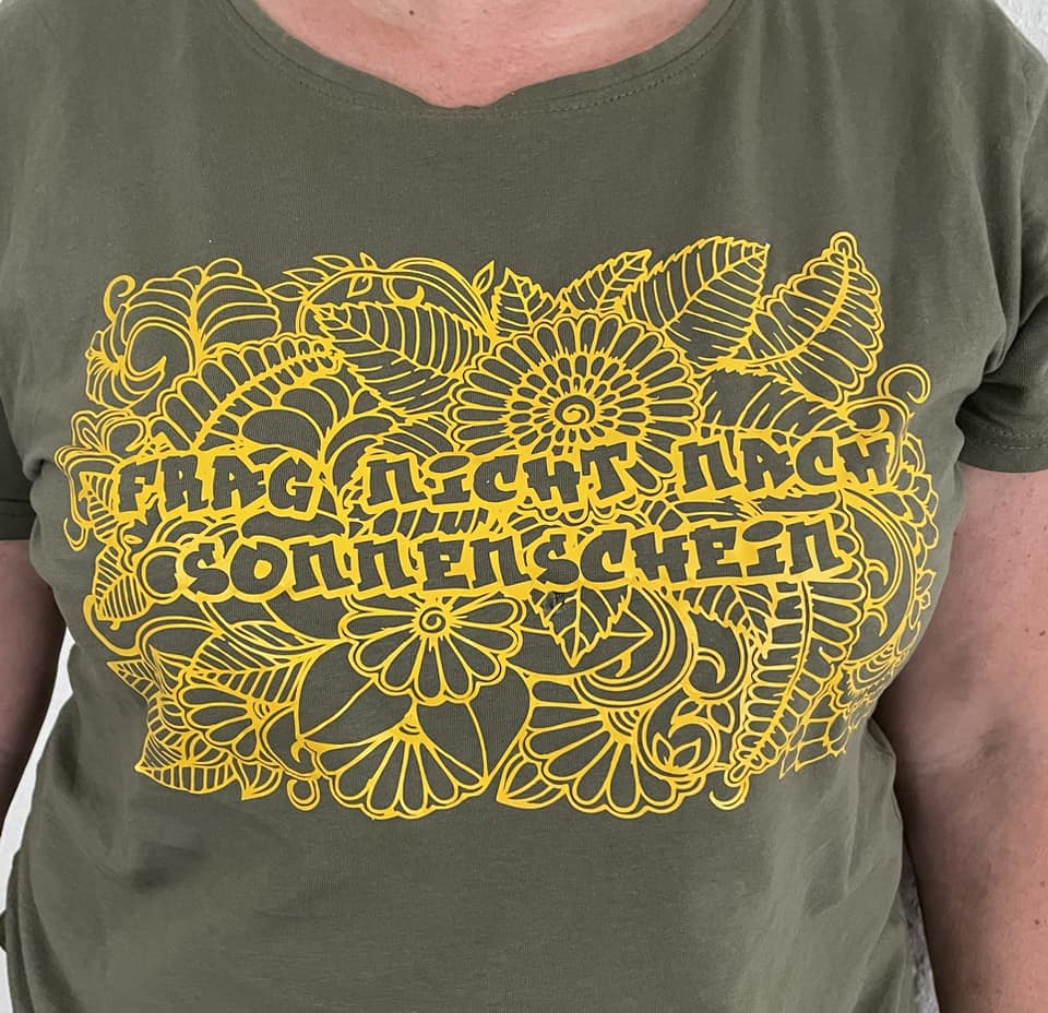 Person trägt ein T-Shirt mit dem Motiv "Frag nicht nach Sonnenschein" in leuchtendem Gelb, entworfen von easy-sticks.