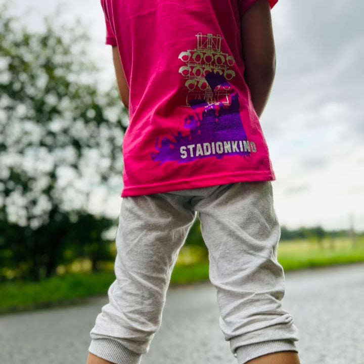 Kind in pinkem T-Shirt mit Stadionkind Aufdruck von easy-sticks, verkörpert Begeisterung für den Fußball, perfekt für junge Fans.