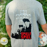Junge in grauem T-Shirt mit SPIEL FÜR SPIEL Aufdruck von easy-sticks, hält einen Fußball, zeigt die Verbindung zur Fußballkultur.