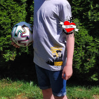 Junge mit grauem T-Shirt und KAMPFEN SIEGEN Aufdruck von easy-sticks, präsentiert seine Fußballbegeisterung und sportlichen Ehrgeiz.