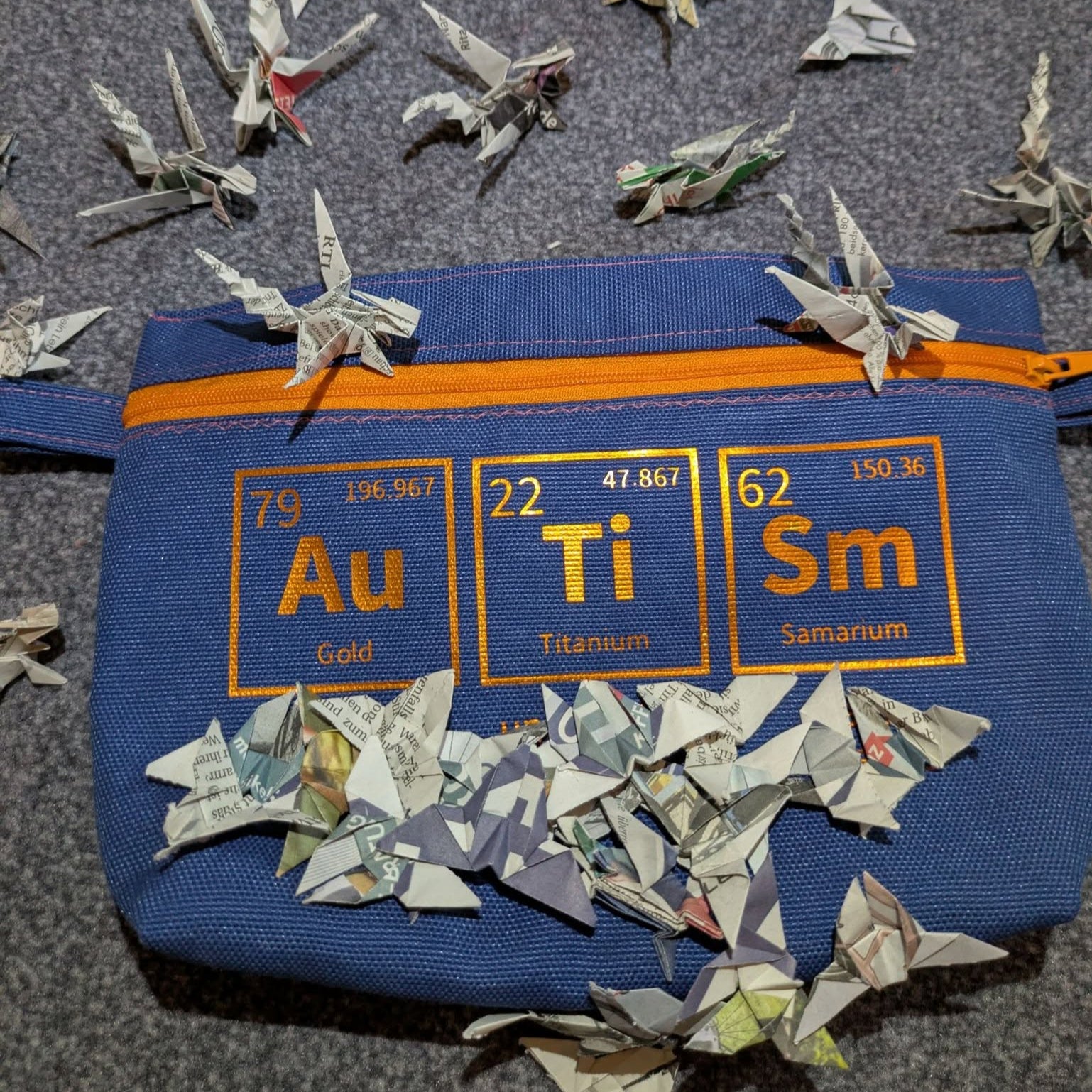 Bunte Tasche mit chemischen Symbolen aus dem Periodensystem von easy-sticks, umgeben von kunstvoll gefalteten Papierfliegern, ein kreatives DIY-Modell.