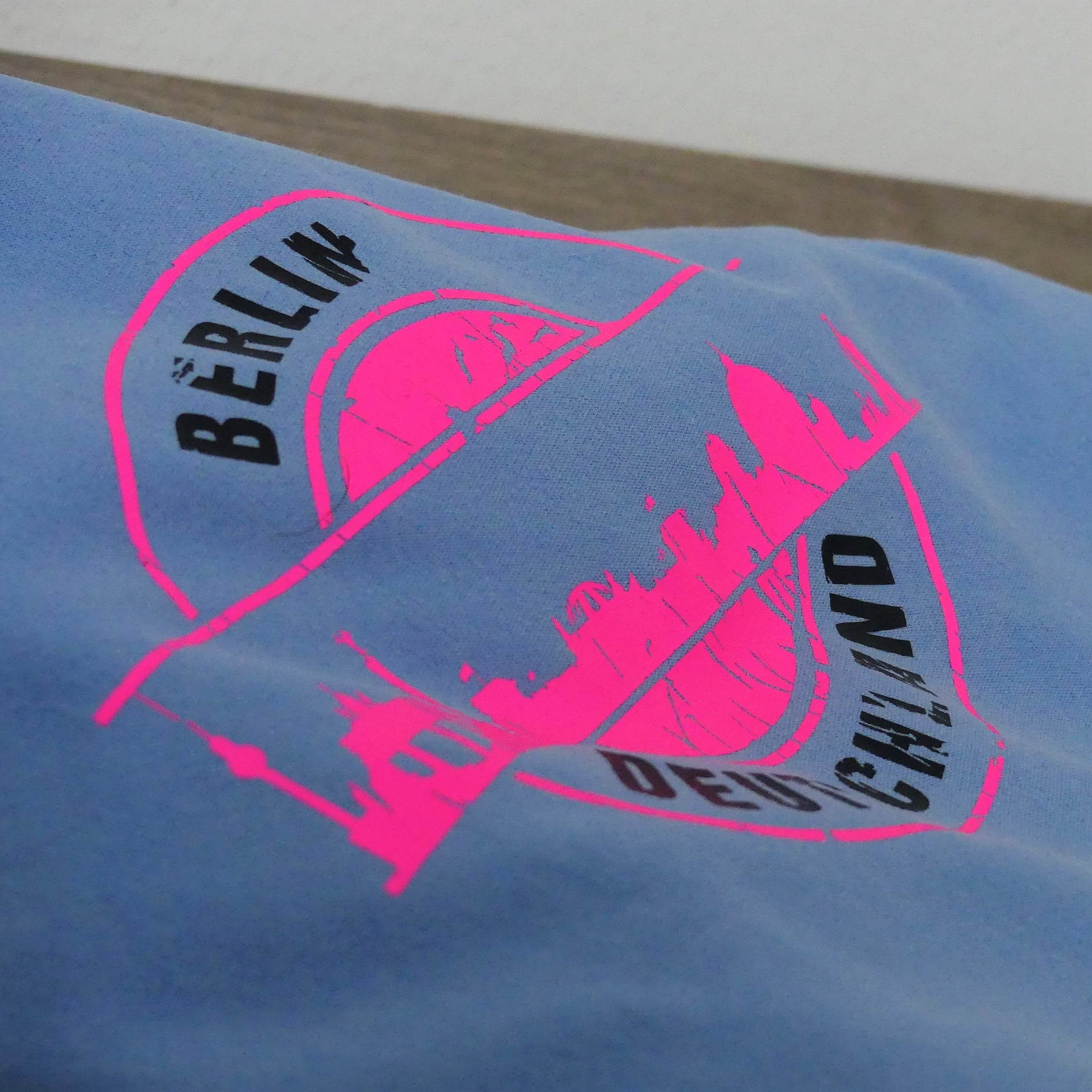 Hellblaues T-Shirt mit leuchtendem, pinkem Druck der Berliner Skyline und dem Schriftzug "DEUTSCHLAND". Eine kreative Verwendungsmöglichkeit mit der Stempel Skyline Berlin Plotterdatei von easy-sticks.