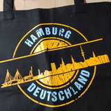 Eine schwarze Tragetasche mit dem Aufdruck der Hamburg Skyline, inspiriert von der "Stempel Skyline Hamburg" Plotterdatei von easy-sticks, perfekt für DIY-Projekte.