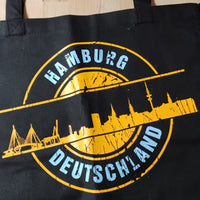 Eine schwarze Tragetasche mit dem Aufdruck der Hamburg Skyline, inspiriert von der "Stempel Skyline Hamburg" Plotterdatei von easy-sticks, perfekt für DIY-Projekte.