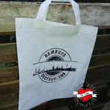 Eine weiße Tragetasche, die die stilisierte Skyline von Hamburg zeigt, erstellt mit der "Stempel Skyline Hamburg" Plotterdatei von easy-sticks, großartig für individuelle Designs.