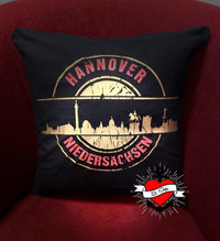 Dekoratives Kissen mit dem Aufdruck "Stempel Skyline Hannover" von easy-sticks. Präsentiert die Skyline von Hannover in goldener Schrift, ideal für kreative Projekte mit der Plotterdatei.