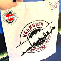 Tragetasche in neutralem Farbton mit dem stilvollen "Stempel Skyline Hannover" Motiv von easy-sticks. Perfekt für personalisierte DIY-Projekte basierend auf der Plotterdatei.
