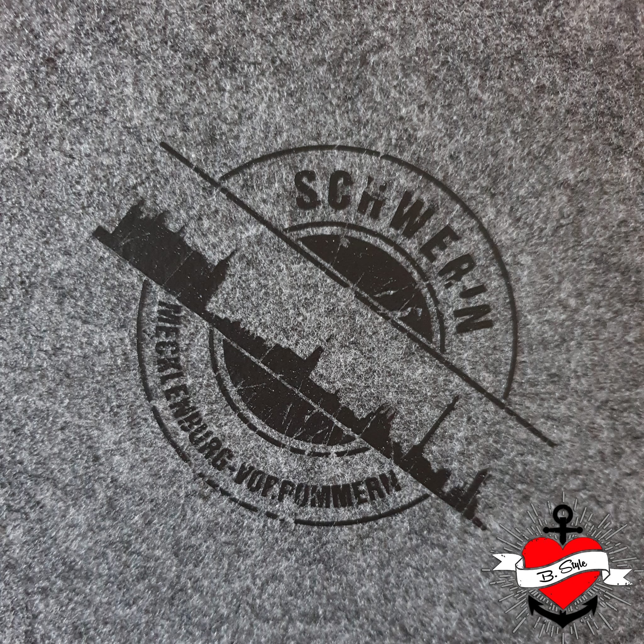Eine minimalistische schwarze Anwendung der "Stempel Skyline Schwerin" Plotterdatei von easy-sticks auf einem grauen Stoff. Ideal für individuelle Projekte.