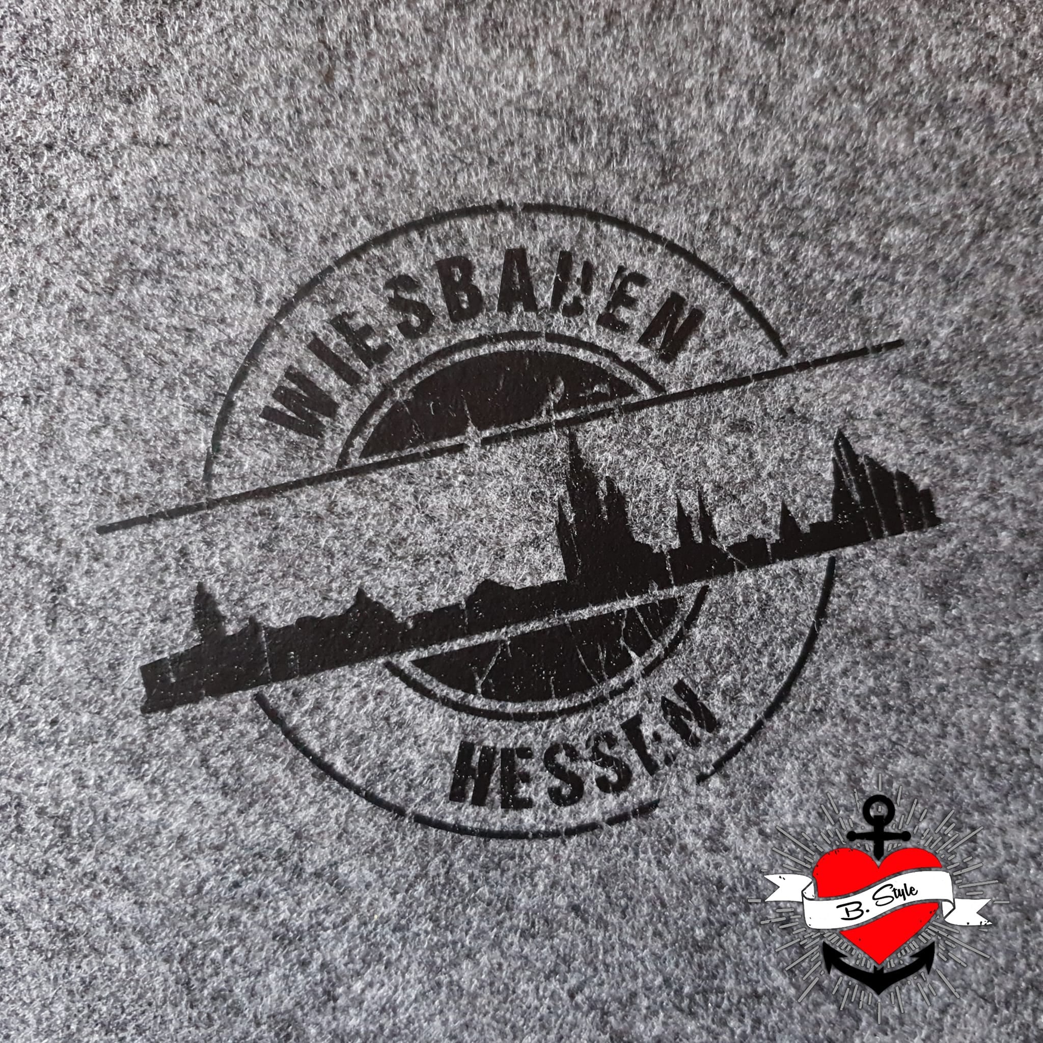 Das stilvolle Design der Skyline Wiesbaden Plotterdatei von easy-sticks auf einem grauen Stoff, präsentiert den Schriftzug 'WIESBADEN HESSEN' in einem eleganten Schwarz.