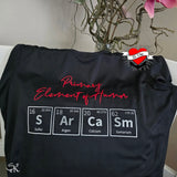 Schwarzes T-Shirt mit dem Slogan 'Primary Element of Humor' und chemischen Symbolen S, Ar, Ca, Sm. Ideal für kreative DIY-Projekte, erstellt mit der Periodensystem Plotterdatei von easy-sticks.