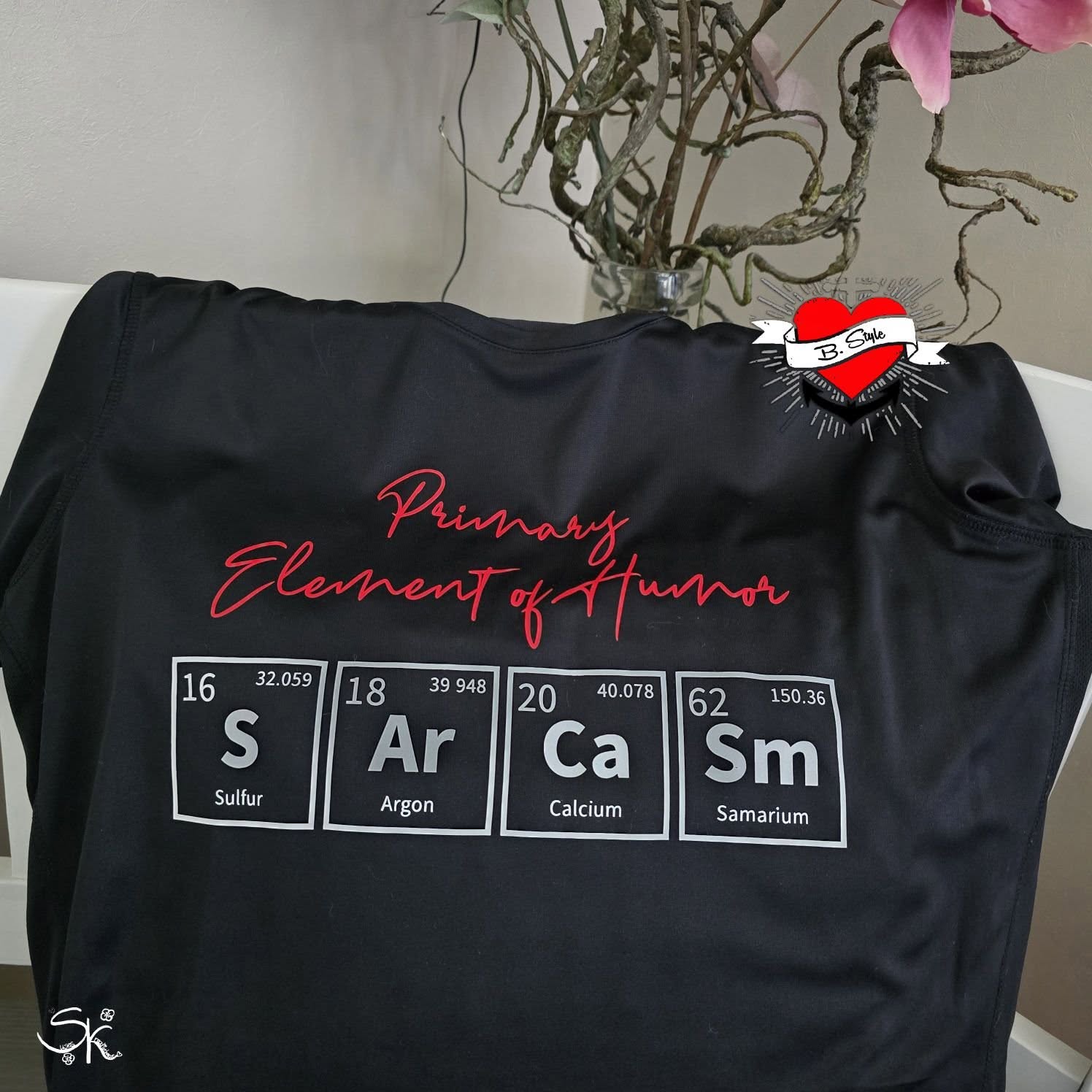Schwarzes T-Shirt mit dem Slogan 'Primary Element of Humor' und chemischen Symbolen S, Ar, Ca, Sm. Ideal für kreative DIY-Projekte, erstellt mit der Periodensystem Plotterdatei von easy-sticks.