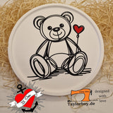 Eine runde Platte mit einem liebevollen Teddy-Motiv und Herz, gestaltet mit der Plotter Datei 'Teddy mit Herz' von easy-sticks. Umgeben von Holzwolle für kreatives Basteln.