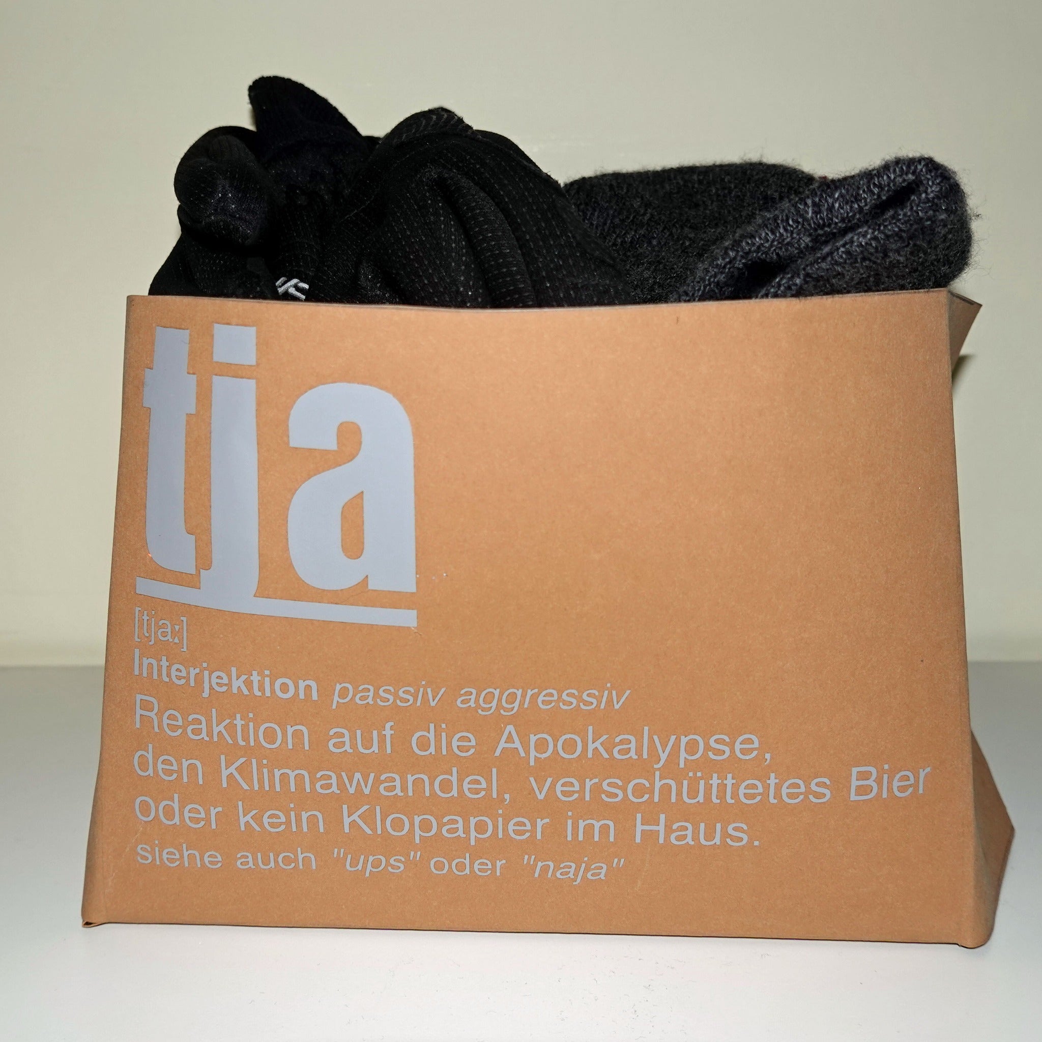 Stylische Aufbewahrung mit der Tja Plotterdatei von easy-sticks, präsentiert in einer kreativen Holzkiste, gefüllt mit schwarzen Textilien und versehen mit einem modernen Design.