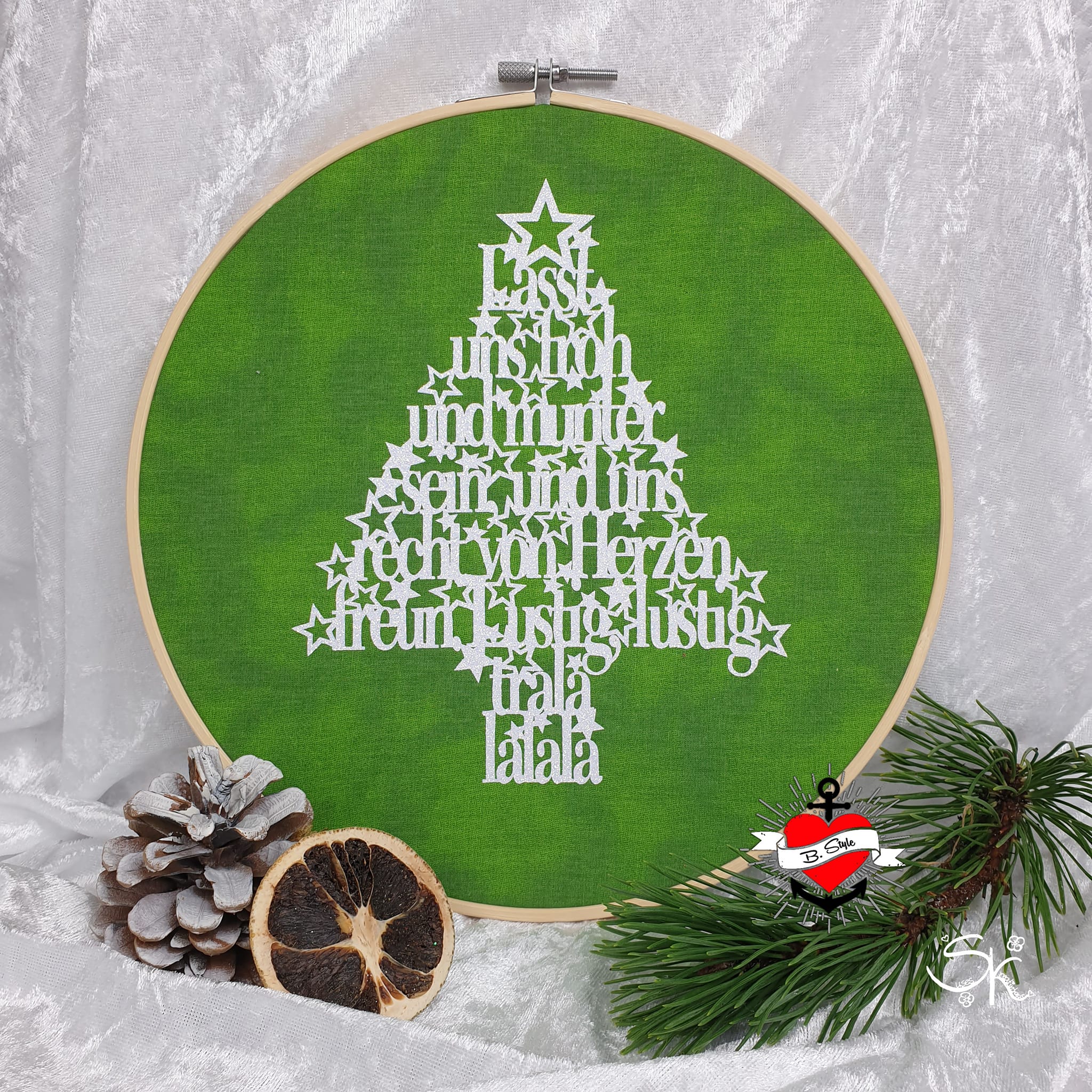 Ein wunderschöner grüner Stickrahmen-Dekoration mit einem Tannenbaum und den Worten "Lasst uns froh und munter sein, und uns recht von Herzen freun. Lustig, lustig, trala lalala" für kreative Weihnachtsideen von easy-sticks.