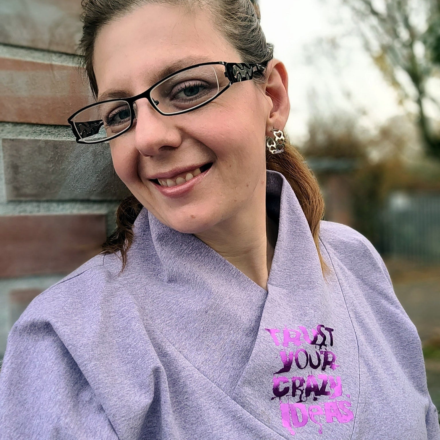 Person, die ein Outfit mit dem Schriftzug 'TRUST YOUR CRAZY IDEAS' von easy-sticks trägt, lächelnd in der Natur.