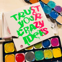 Farbige Malerei mit dem Slogan 'TRUST YOUR CRAZY IDEAS' von easy-sticks, dargestellt auf einer blanken Leinwand.