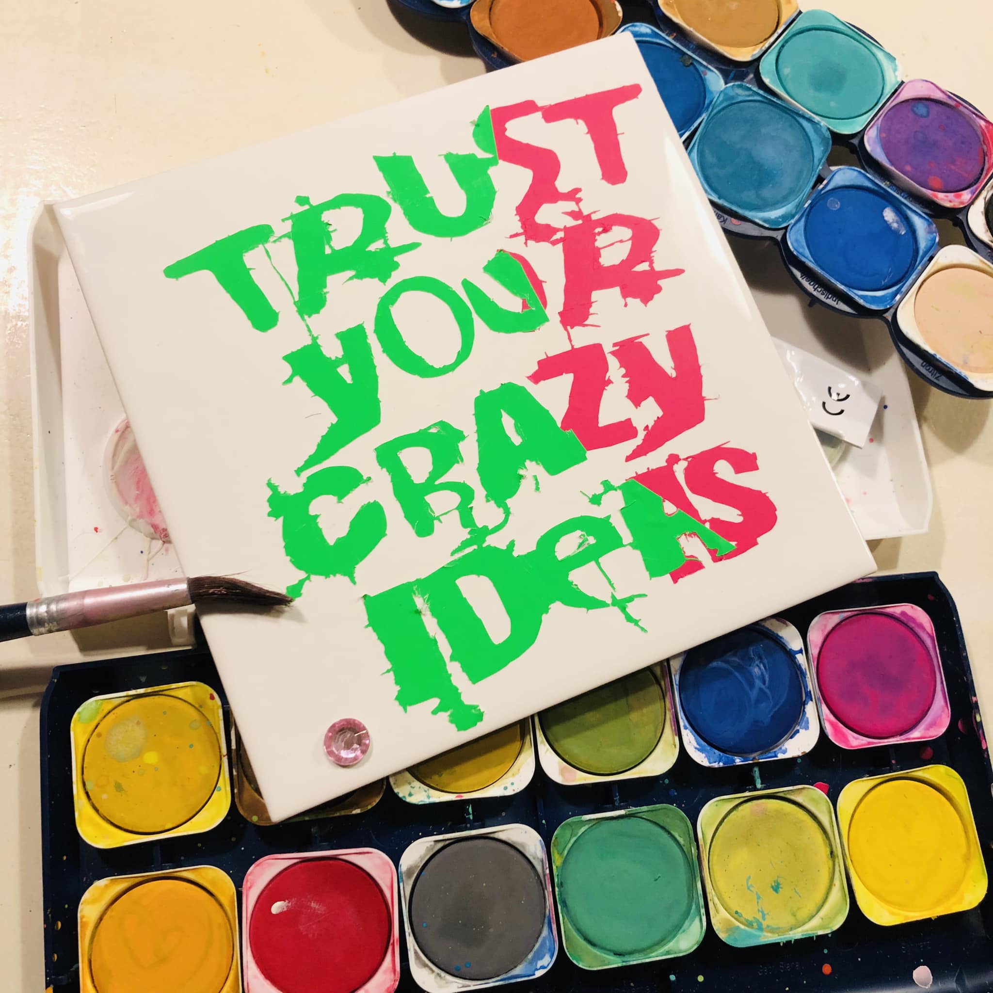 Farbige Malerei mit dem Slogan 'TRUST YOUR CRAZY IDEAS' von easy-sticks, dargestellt auf einer blanken Leinwand.