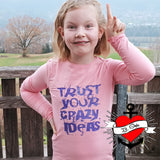 Ein glückliches Mädchen in einem rosa Shirt mit dem Schriftzug 'TRUST YOUR CRAZY IDEAS' von easy-sticks, das Spaß an kreativen Aktivitäten hat.
